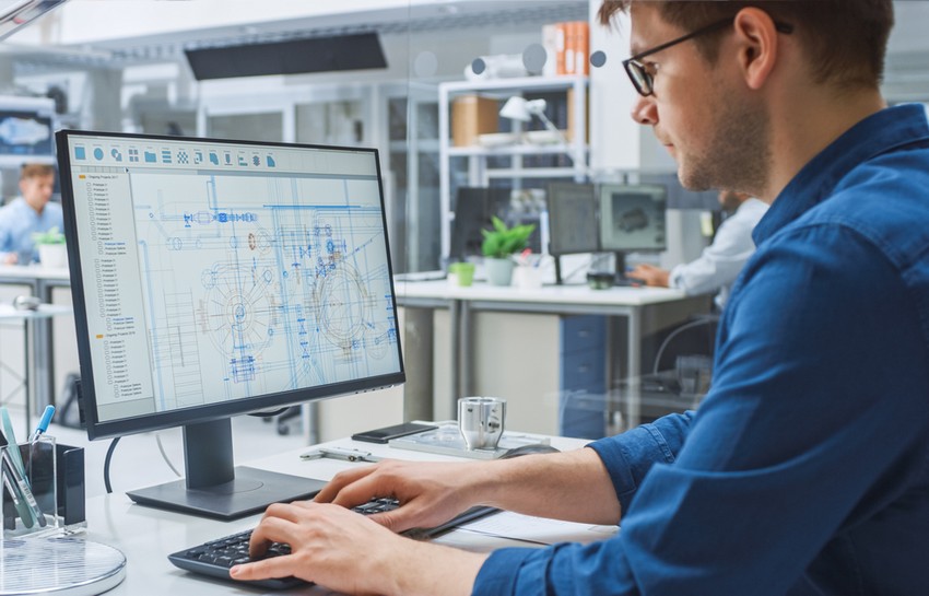 Over the Shoulder Shot of Engineer Working with CAD Software on Desktop Computer, Screen Shows Technical Drafts and Drawings. In the Background Engineering Facility Specialising on Industrial Design